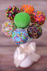 Sweet cake pops in vase on wooden background