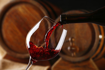 Pouring red wine from bottle into glass with wooden wine casks