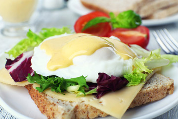 Toast with egg Benedict and tomato on plate on wooden table