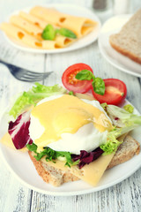 Toast with egg Benedict and tomato on plate on wooden table