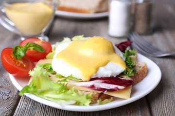 Toast with egg Benedict and tomato on plate on wooden table
