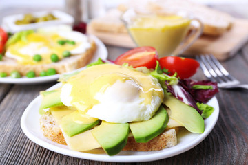 Toast with egg Benedict and avocado on plate on wooden table