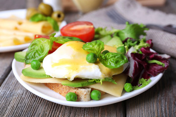 Toast with egg Benedict and avocado on plate on wooden table