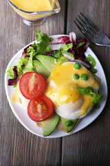 Toast with egg Benedict and avocado on plate on wooden table