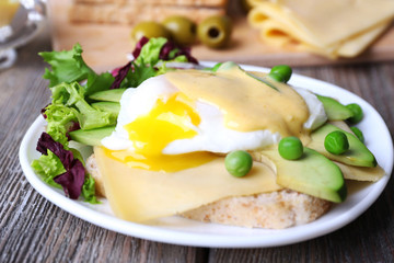 Toast with egg Benedict and avocado on plate on wooden table