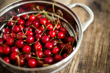 Sweet cherries in colander on color wooden background