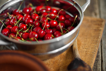 Sweet cherries in colander on color wooden background