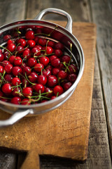 Sweet cherries in colander on color wooden background
