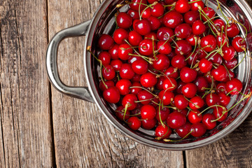 Sweet cherries in colander on color wooden background