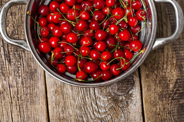 Sweet cherries in colander on color wooden background