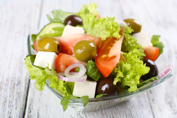 Greek salad in glass dish on color wooden table background