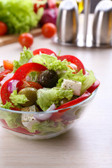 Greek salad in glass dish on wooden table background