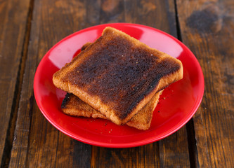 Burnt toast bread on red plate, on wooden table background