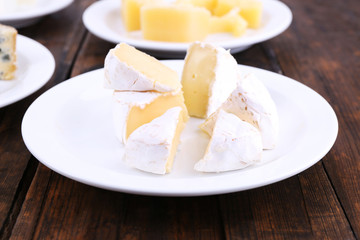 Various types of cheese on plates on wooden table background