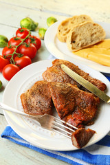 Roasted meat and vegetables on plate, on wooden table