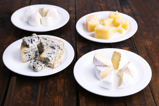 Various types of cheese on plates on wooden table background