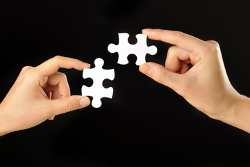 黒い背景で白いパズルのピースを持っている人間の手