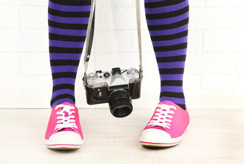 Girl in sneakers with retro photo camera in room