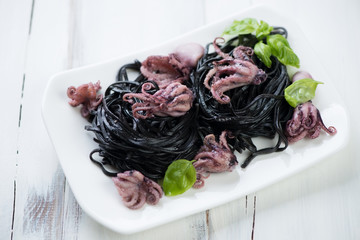 Squid ink colored tagliatelle with octopuses and green basil