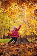 happy child girl throwing leaves in autumn park and laughing