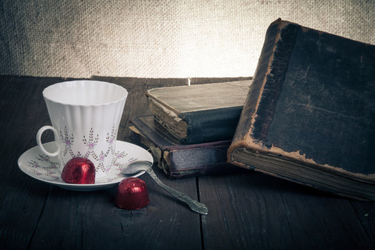 Cup of coffee, shokolad and stack of old books on the old wooden