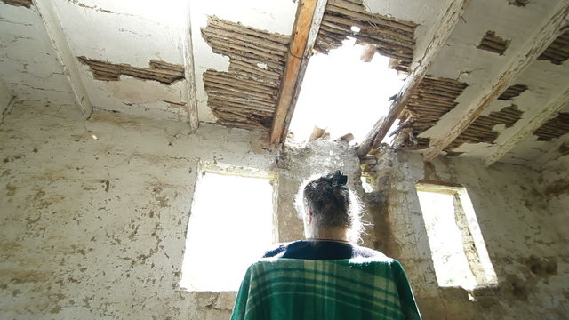Senior person in ruined house looking out the window
