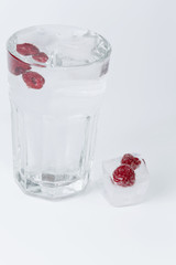 glass of water ice raspberries on a white background