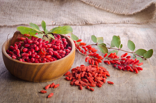 Barberry with leaves and dry goji berries on wooden background
