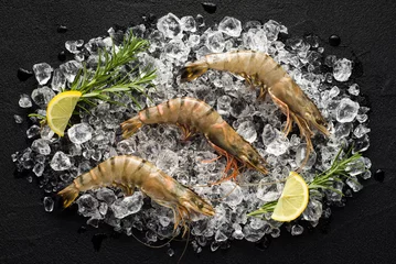 Poster Fresh tiger shrimp on ice on a black stone table top view © nioloxs