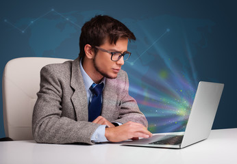 Handsome man sitting at desk and typing on laptop with abstract