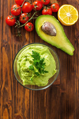 Guacamole on wooden table surrounded by its ingridients