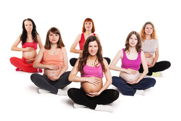 Group of smiling pregnant women sitting on the floor and