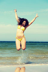 Beautiful woman in swimsuit jumping over seaside.