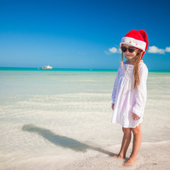 Little adorable girl in red Santa hat at tropical beach