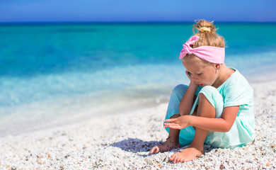 Little adorable girl talking at phone during beach vacation