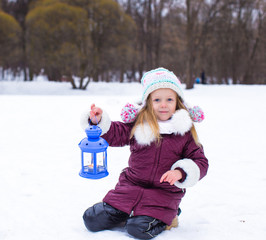 Little girl warms her hands on candle in the lantern outdoors