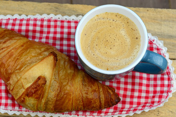 Coffee with croissant on old wooden table and checkered doily