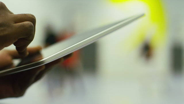 Hands using a tablet during a basketball game in the background