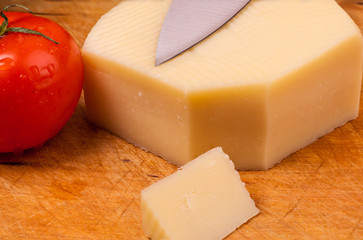 Piece of cheese with a tomato on a wodden board