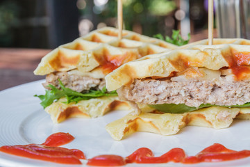 Hamburger made with waffles and pork on white plate.
