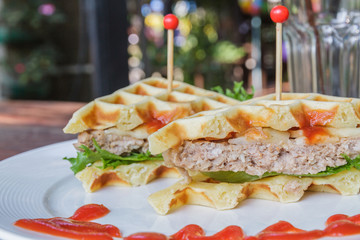 Hamburger made with waffles and pork on white plate.