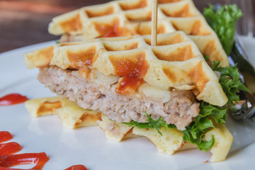 Hamburger made with waffles and pork on white plate.