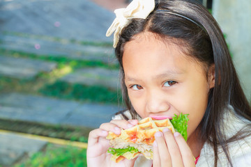 Asia child girl eating Hamburger made with waffles and pork.