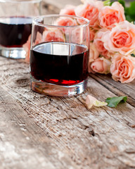 Glasses of Red Wine and Pink Roses on Wooden Background