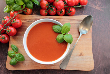 Tomato soup in a bowl on wooden board with spoon