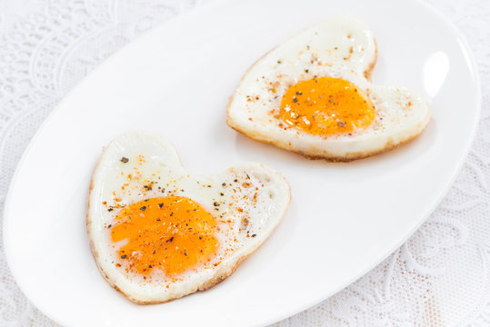 Fried eggs in the form of heart on white plate