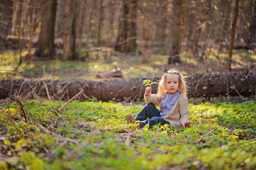 Naklejka na ściany i meble cute blonde child girl sitting in green spring forest