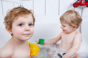 Two little sibling boys having fun with water by taking bath in