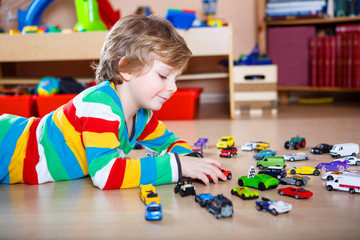 Happy funny little blond child playing with lots of toy cars