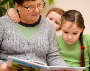 Grandmother is reading book with her grandchildren